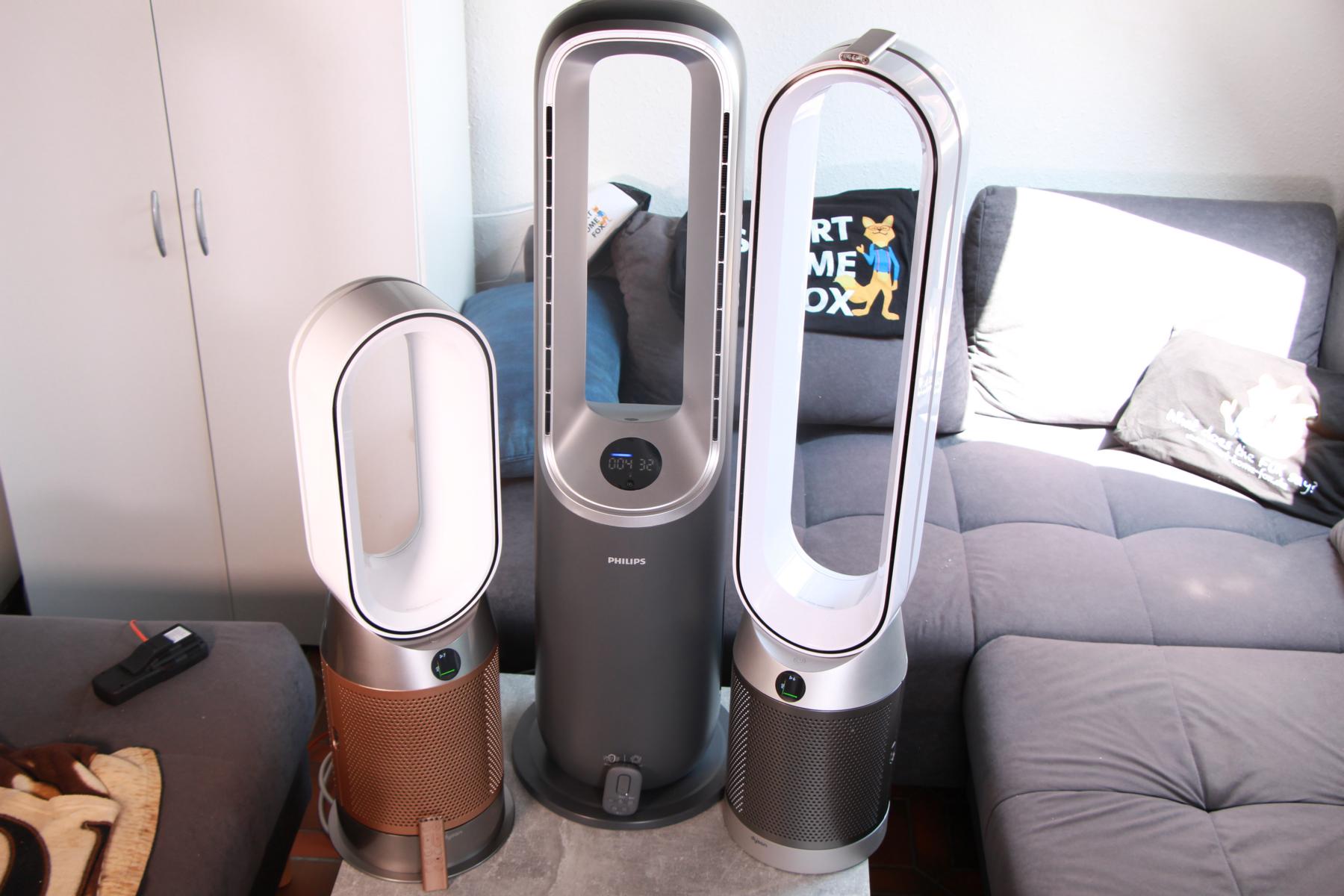 Der Philips Air Performer Series 8000 Luftreiniger, Ventilator und Heizlüfter steht im Test neben 2 Dyson Kombigeräten im direkten Vergleichauf einem Tisch vor einer Couch.